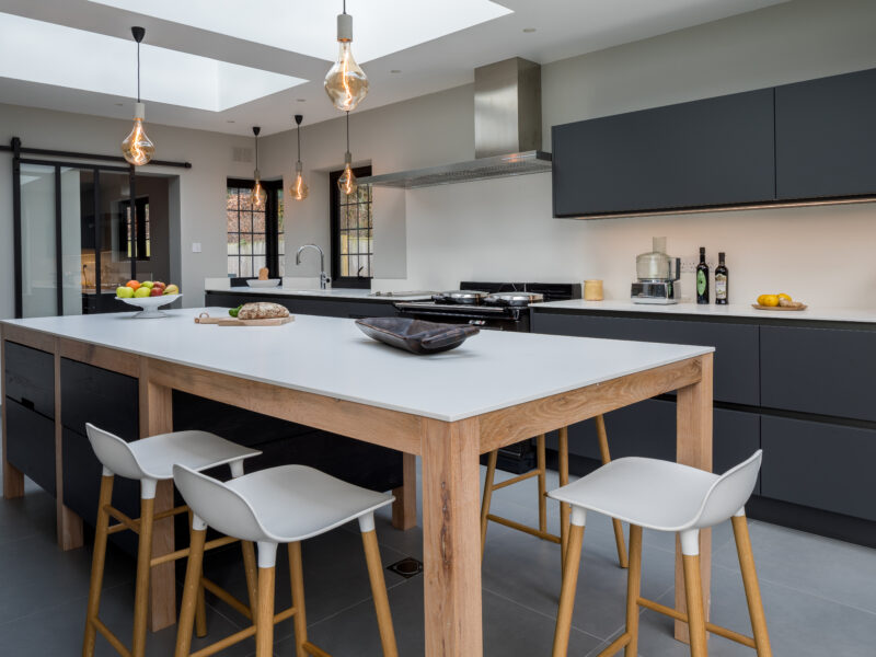 Bright kitchen with light oak island, white worktop, black cabinetry and copper pendant lights