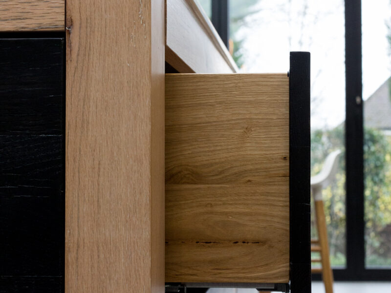 Dovetail drawer detail in mixed oak tones with black handles and a garden view