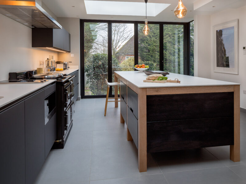 Dark-stained oak island with copper pendants in front of black bifold doors onto the garden