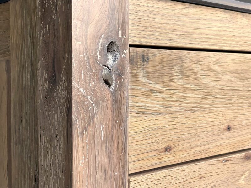 Wood grain detail with prominent knots on a light oak drawer front with black handle