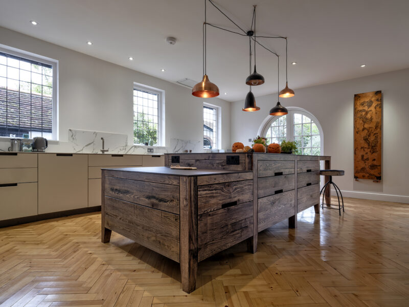 Dark-stained oak island with pale grey worktop in a sage-toned kitchen
