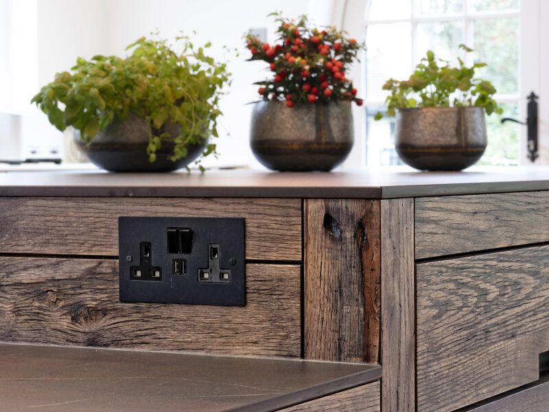 Close-up of a dark oak island end with integrated socket and flowering plants