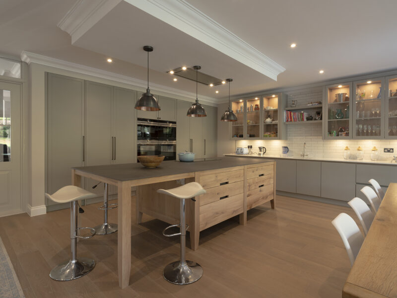 Reclaimed oak island with grey worktop, cream cabinetry and three dark pendant lights on parquet