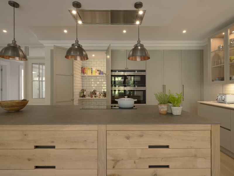 Light oak island with grey worktop framed by cream cabinetry and white subway tiles