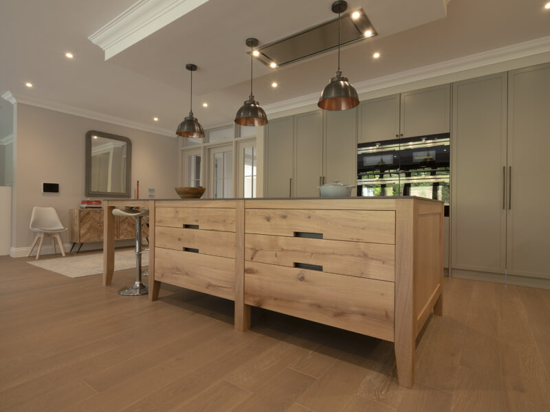 Light oak island on herringbone parquet with grey worktop and a brass pendant cluster